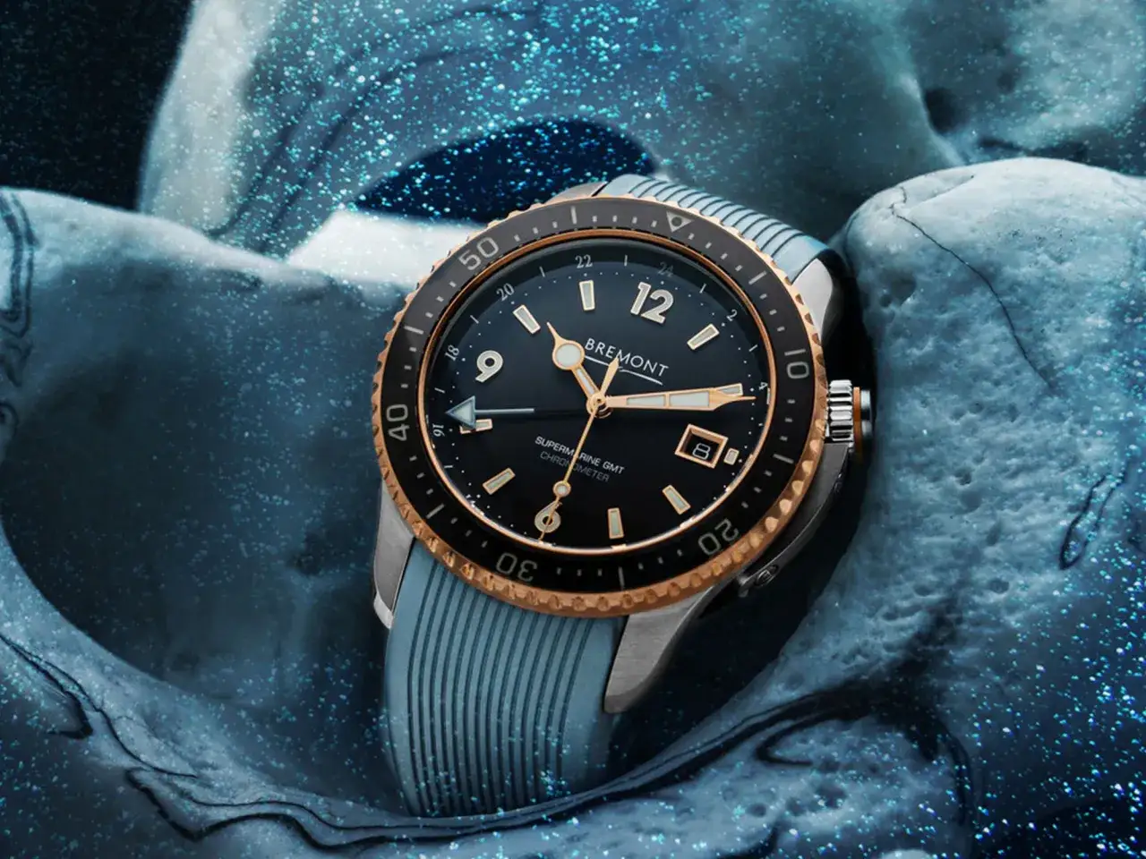 Orologio Bremont Supermarine GMT, con lunetta in bronzo e cinturino blu, immerso in un ambiente acquatico scintillante. Il suo significato &egrave; legato al viaggio e al tempo.
