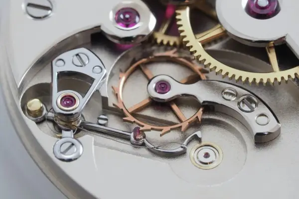 Meccanismo di orologio con ingranaggi dorati e ruota bilanciere, parte di uno scappamento coassiale.
