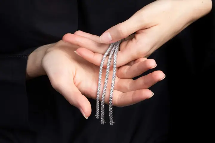 Mani delicate tengono tre scintillanti bracciali tennis, un classico intramontabile la cui storia affonda le radici nel mondo dello sport.
