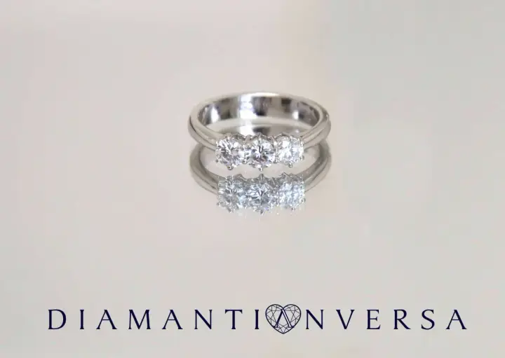 Un anello prezioso con tre diamanti scintillanti, riflesso su una superficie lucida.