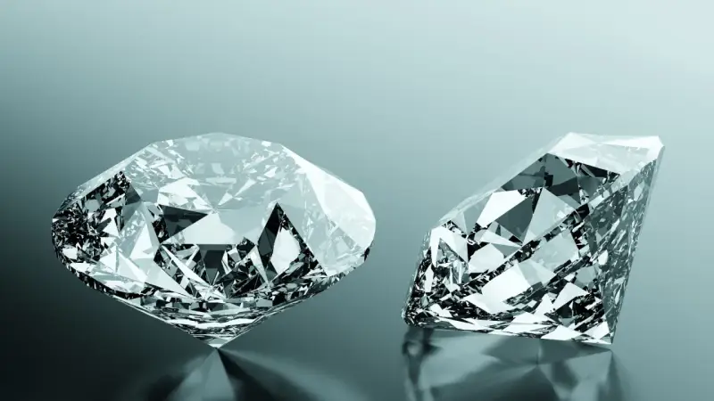 Due diamanti scintillanti, uno rotondo e uno a goccia, riflettono la luce. Uno dei due, un diamante brown, brilla con sfaccettature perfette.